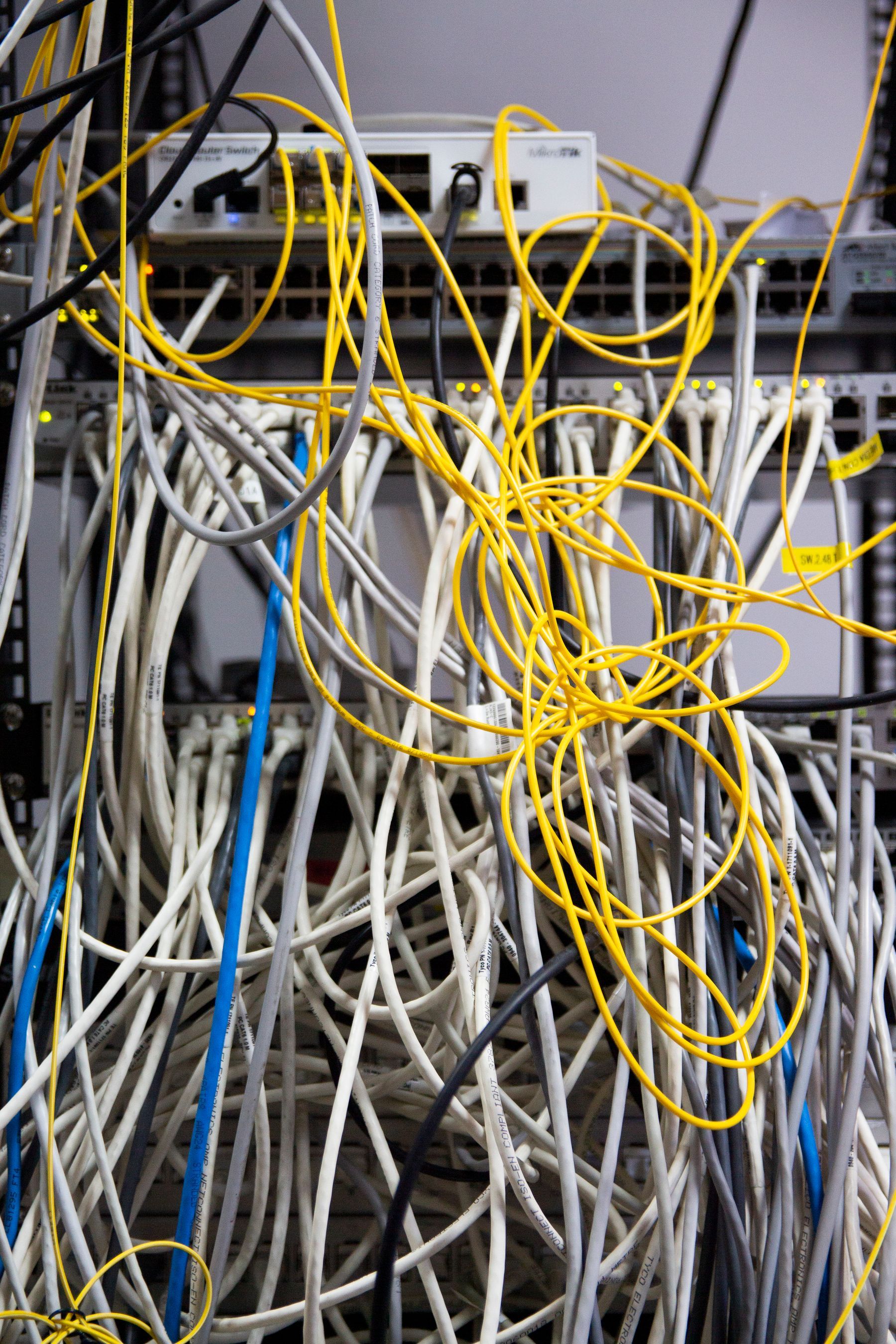Tangle of unmanaged white and yellow patch cables hanging in front of network switches