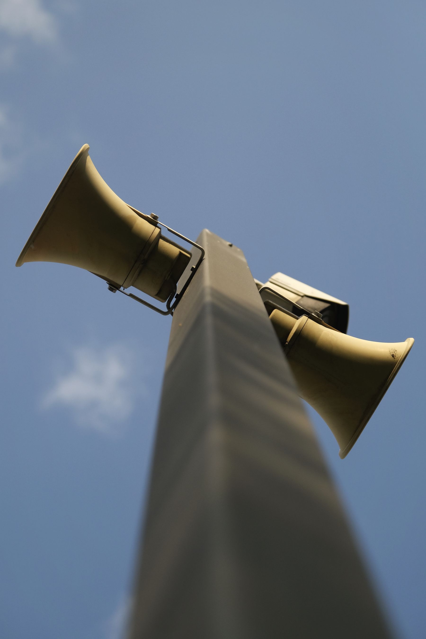 Pair of horn loudspeakers mounted on a metal pole, seen from below against the sky