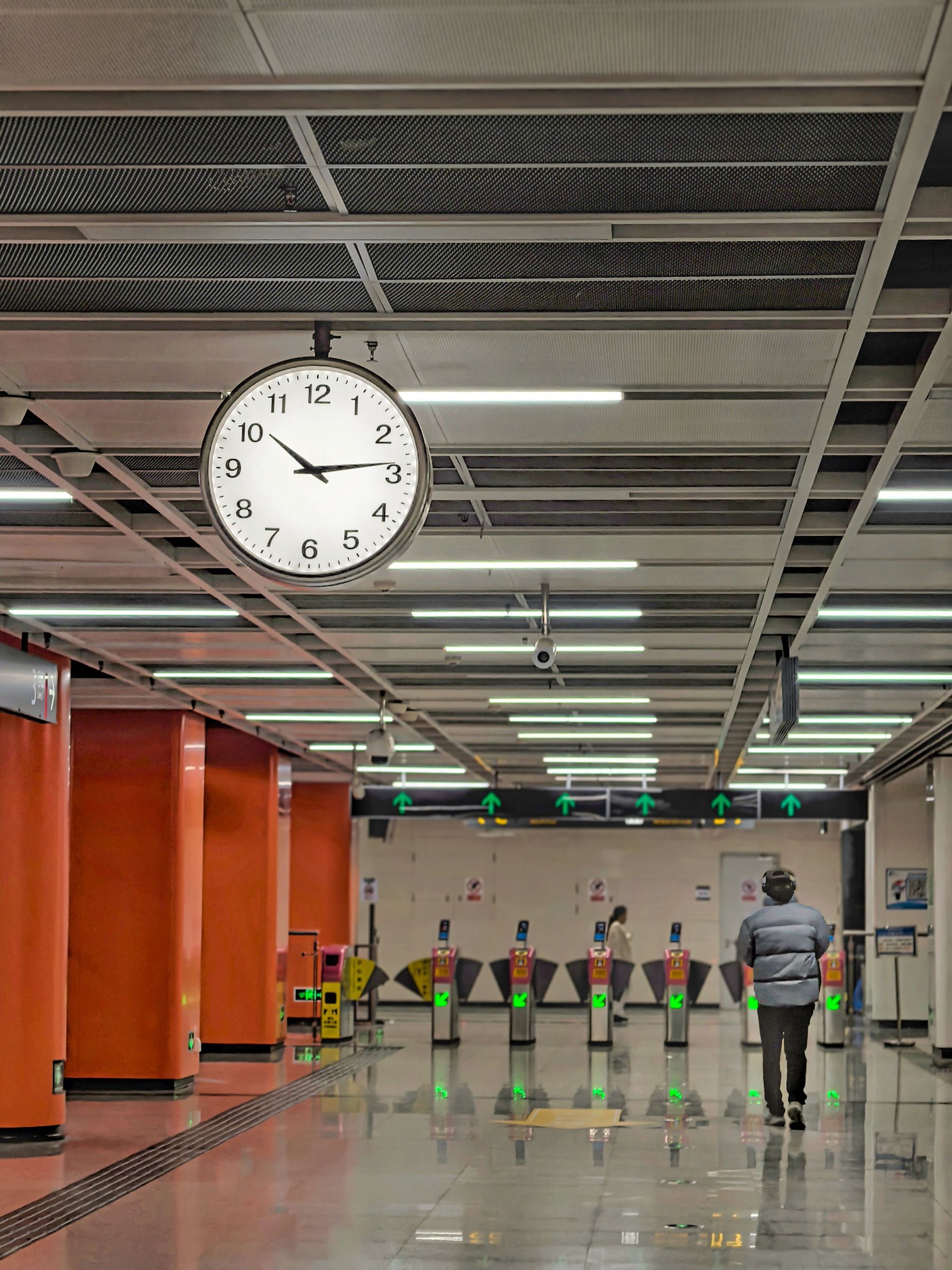 Large double faced analog clock hanging from the ceiling of a transit station concourse