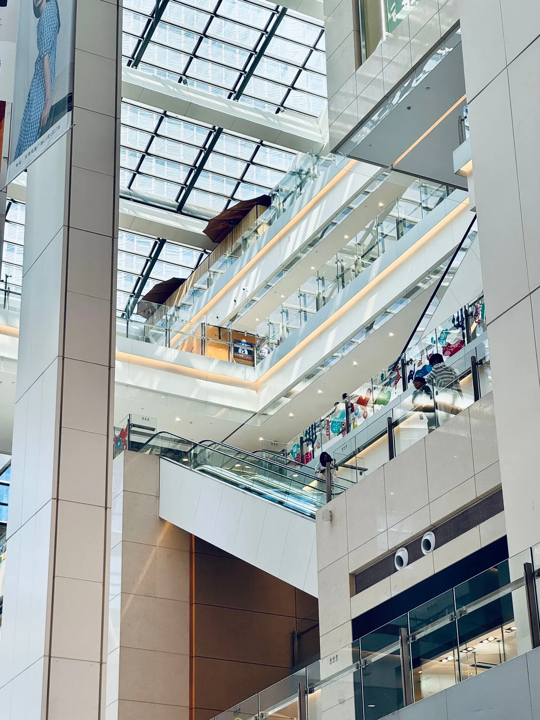 Multi level shopping mall interior with escalators, glass ceiling and bright lighting